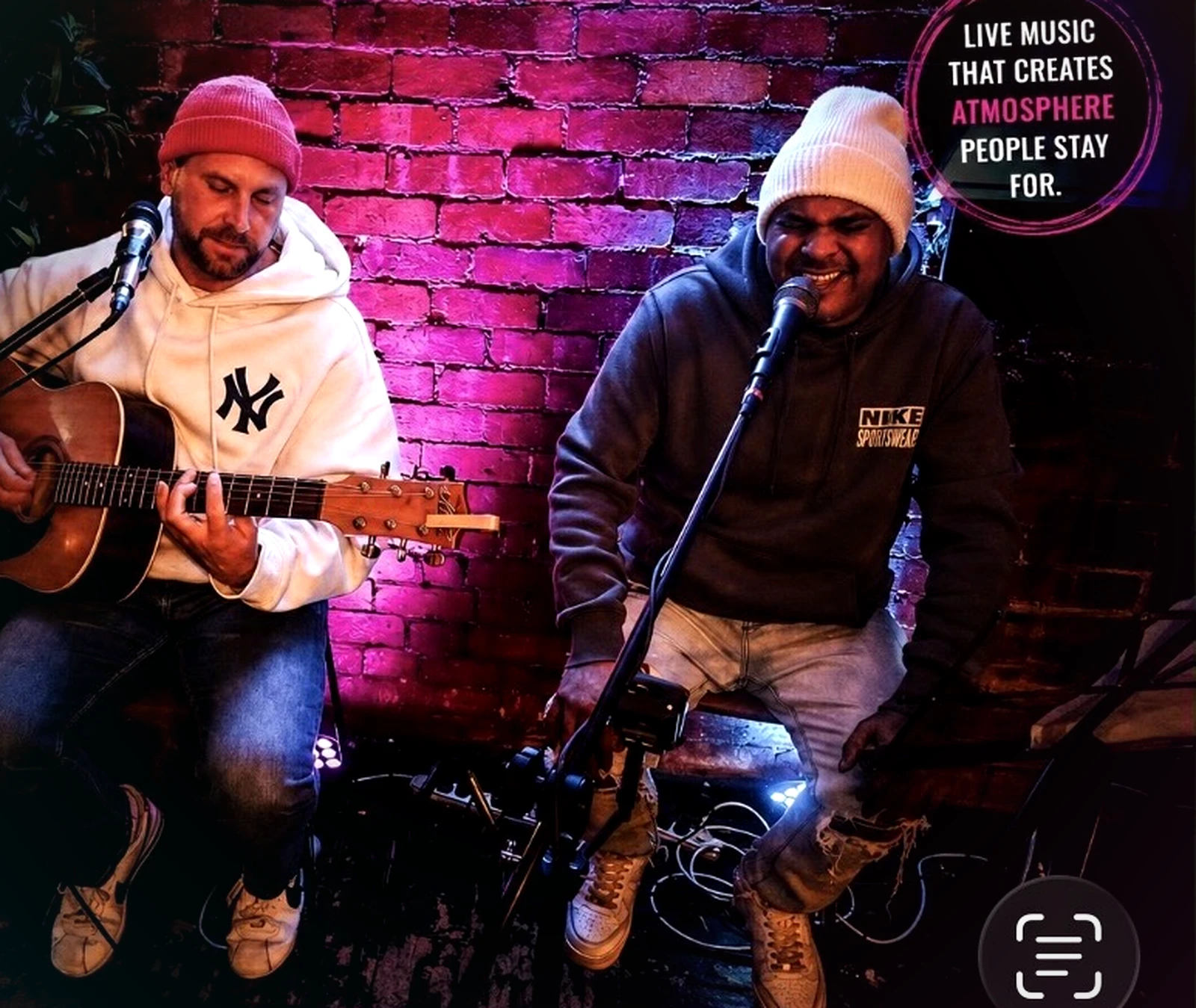 Wiz on acoustic guitar and Dash on the mic against a magenta-lit brick wall